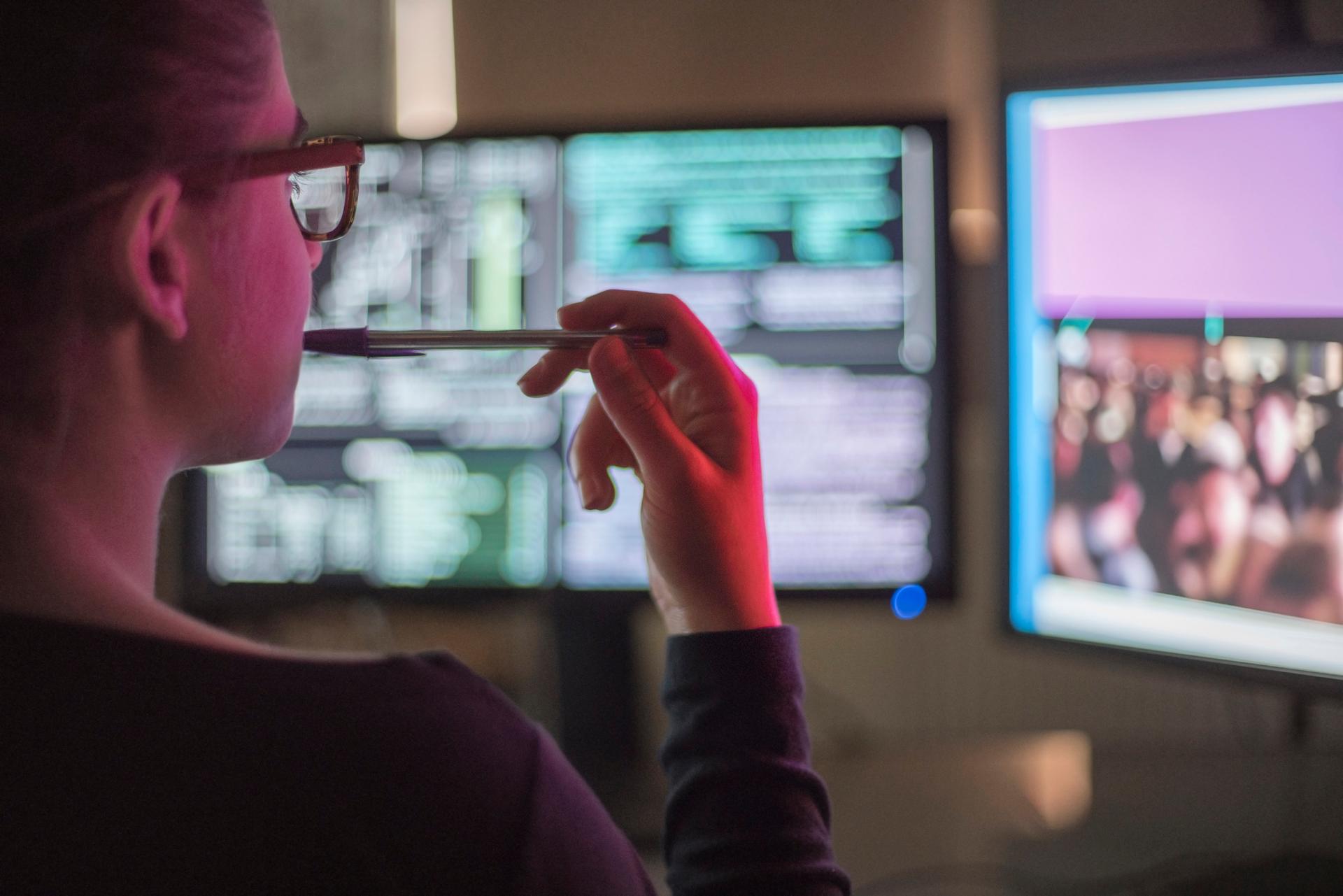 person watching screens and biting pen