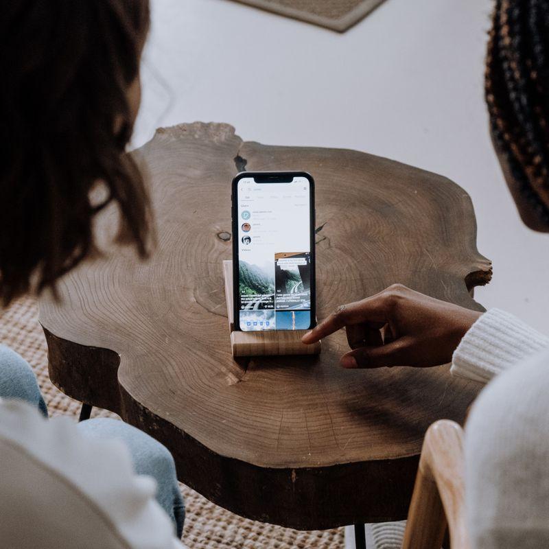 2 people watching a phone on a small wooden table