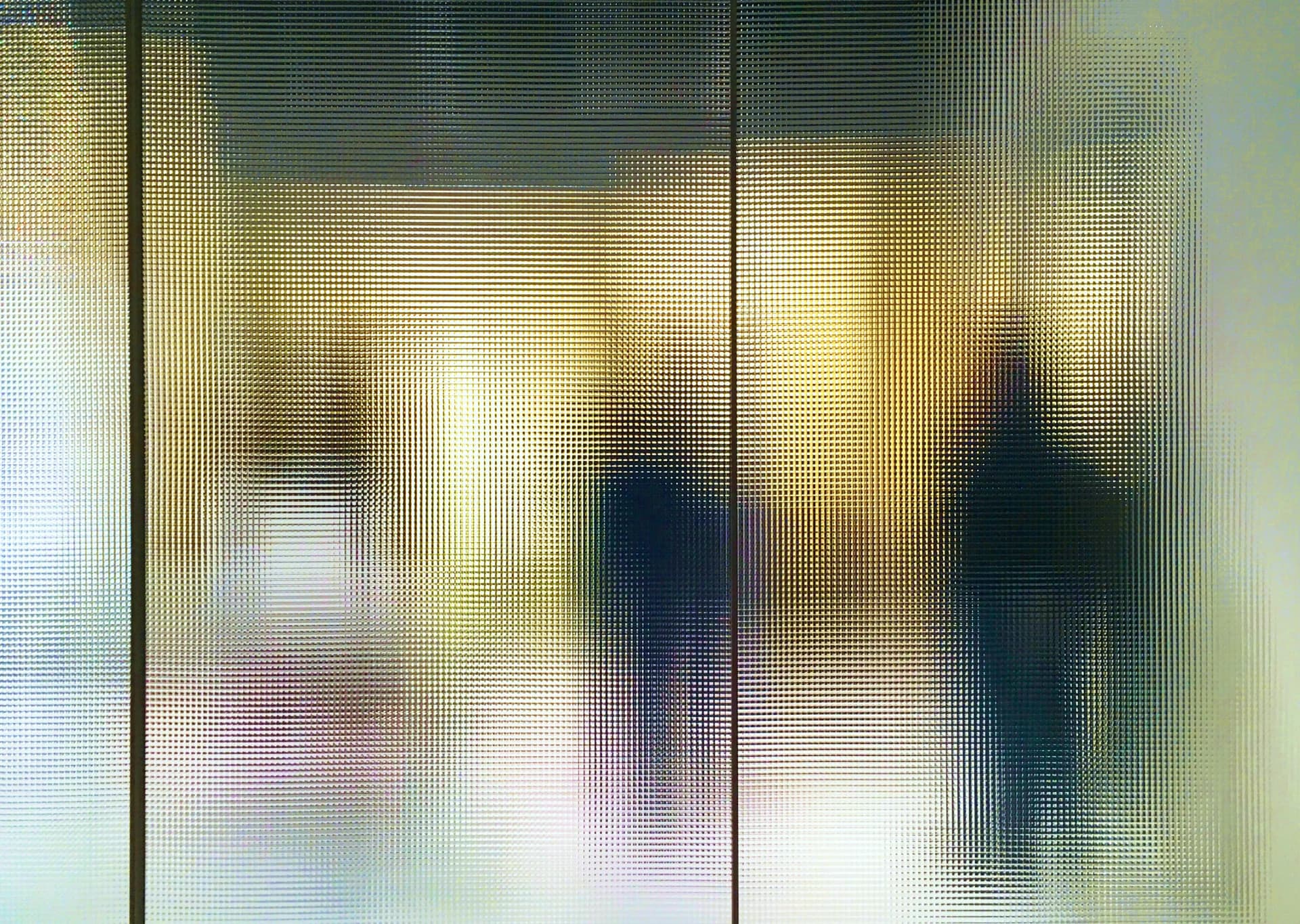 Blurry silhouettes of people are seen through frosted glass, creating an abstract, mysterious appearance with yellow and gray tones.