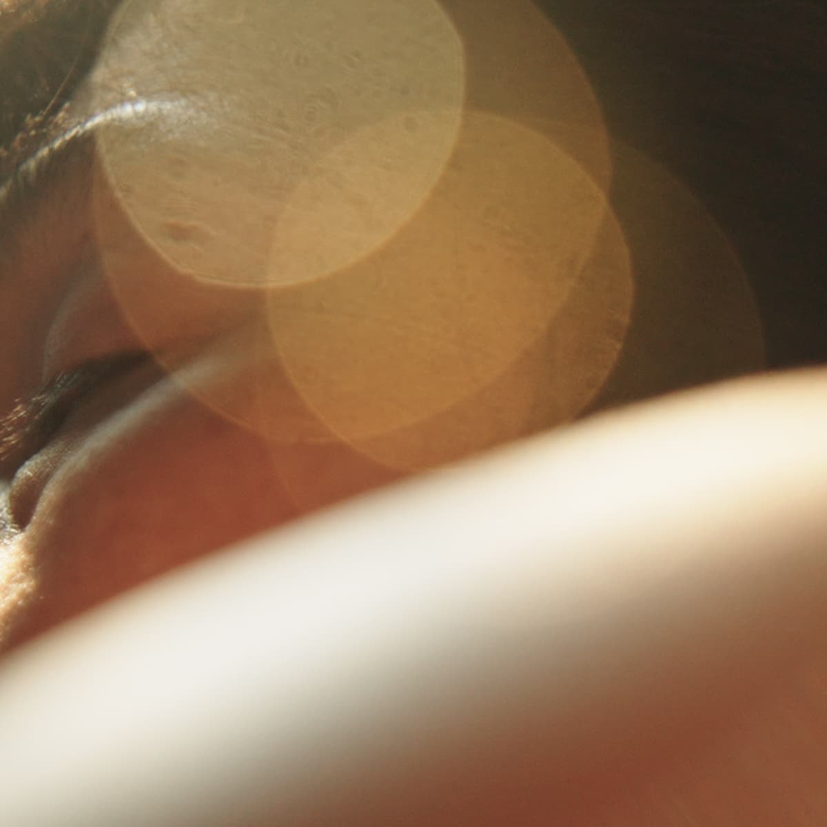 Close-up of a person's face, partially visible, with soft focus and warm lens flares creating an ethereal effect.