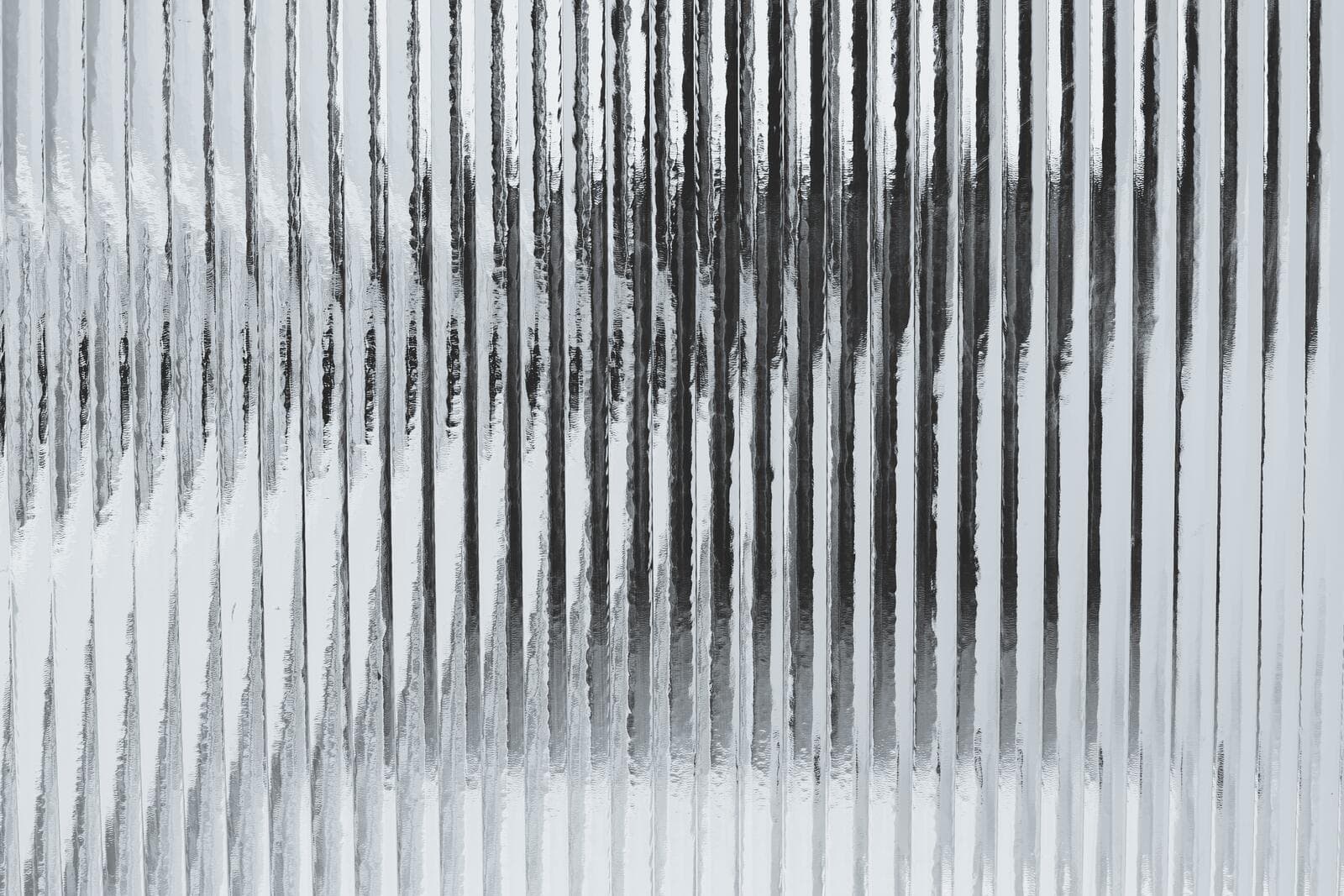 A close-up of a textured, corrugated glass surface with vertical ridges, creating a distorted reflection of light and shadow.