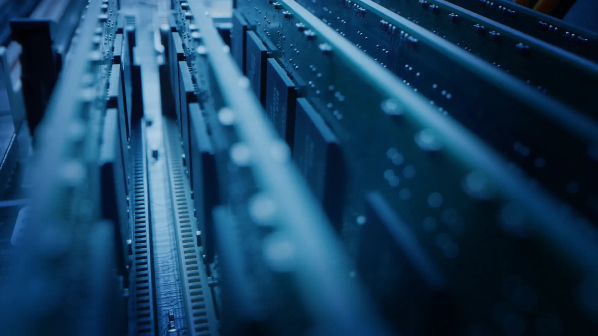 Close-up of blue-lit computer circuit boards aligned in parallel rows, showing intricate connections and electronic components.