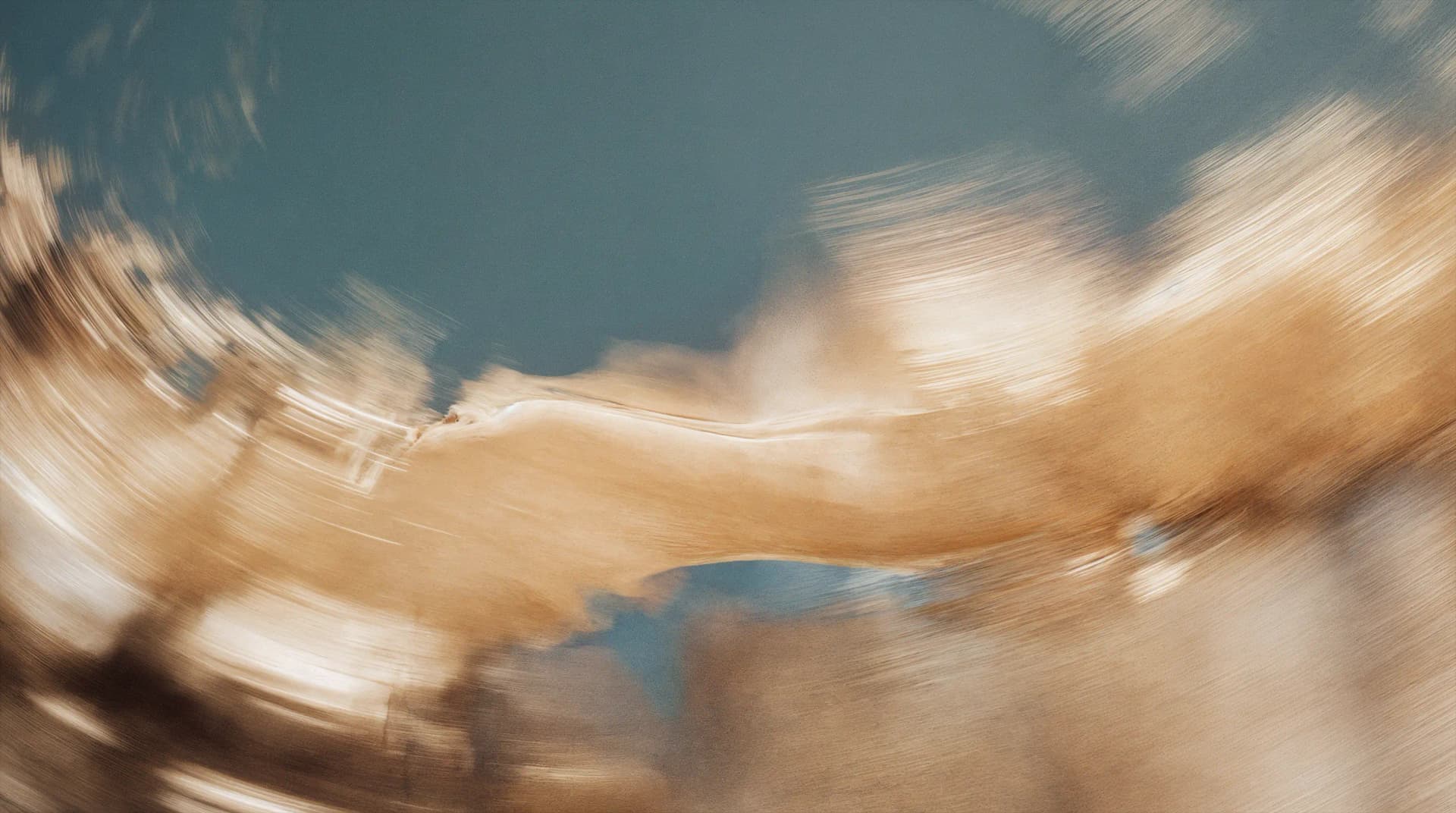 Abstract image with swirling motion of brown and beige hues blending into a dark blue background, creating a fluid, dynamic effect.